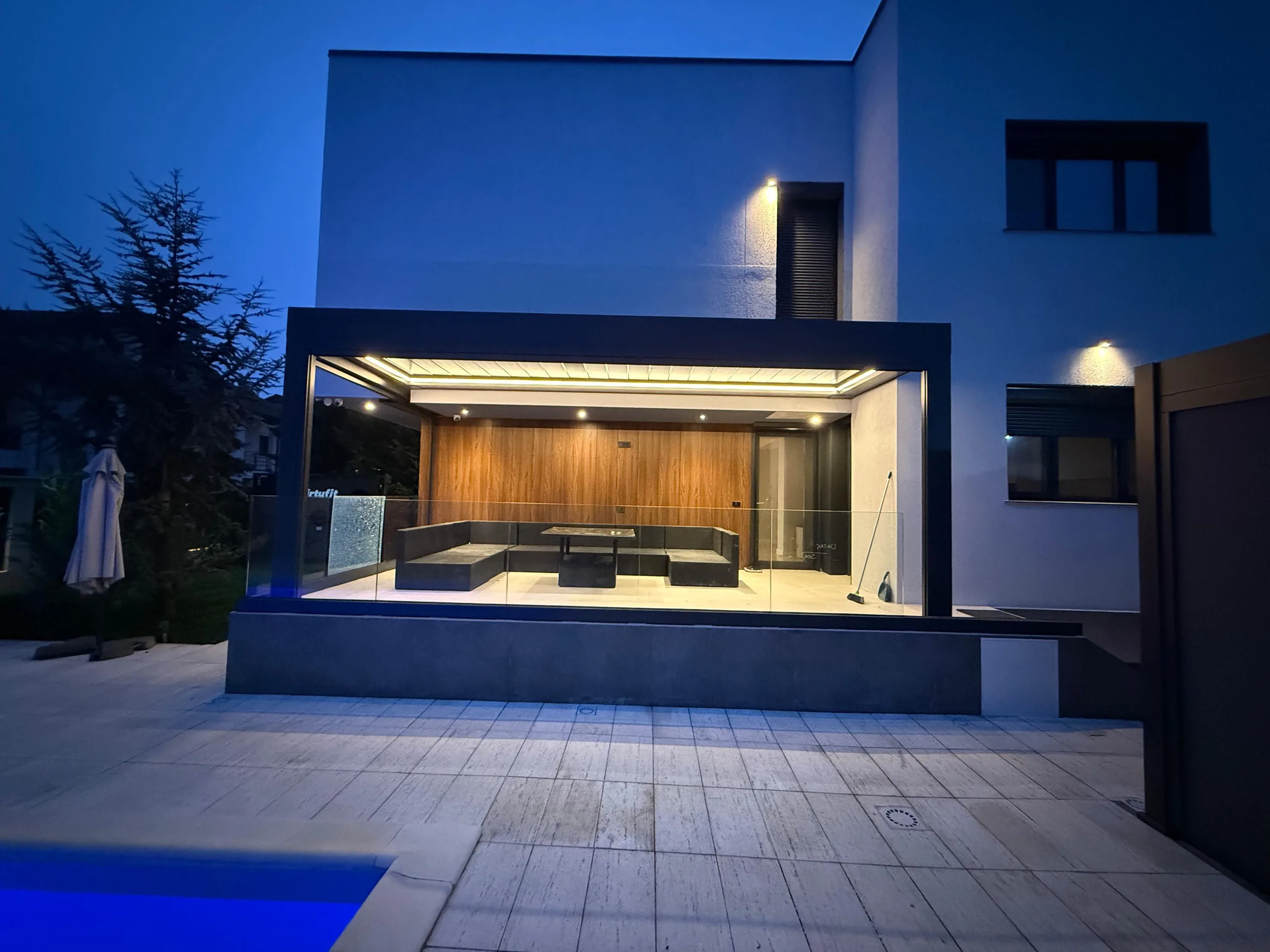 Terasă acoperită cu structură de aluminiu antracit și balustradă din sticlă, iluminată cu LED cald