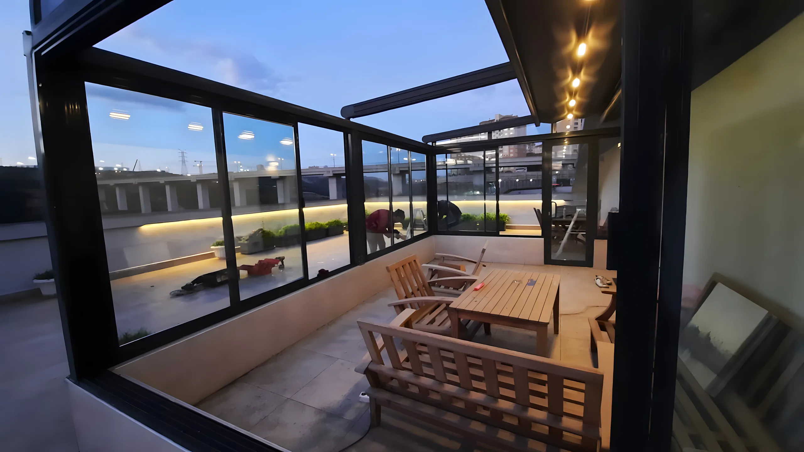 Interiorul unei grădini de iarnă din aluminiu și sticlă, cu spoturi LED și mobilier de lemn