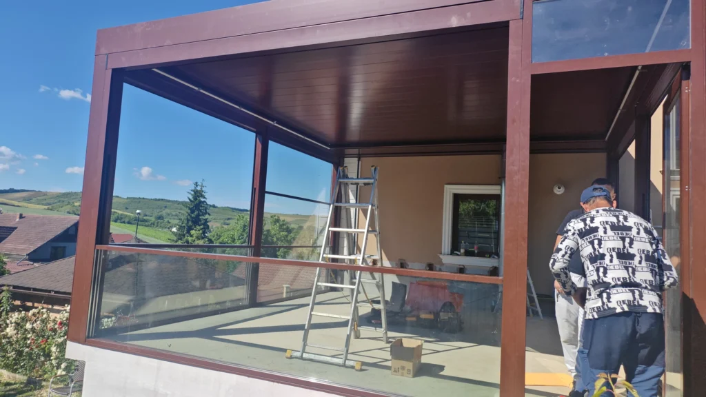 Închidere de terasă cu profile de aluminiu și panouri mari de sticlă glisantă, cu vedere spre dealuri cu vii