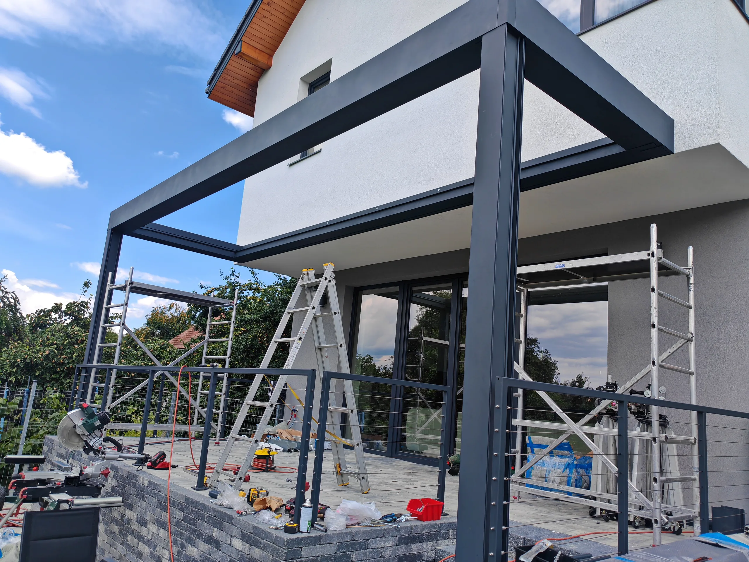 Structură de pergolă din aluminiu antracit ancorată pe fațada unei case